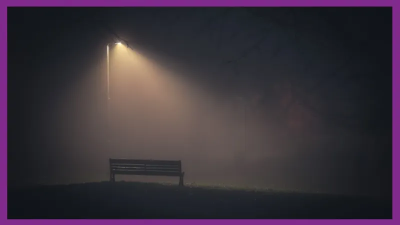 A bench in the distance under a streetlamp with a mass of fog surrounding it.