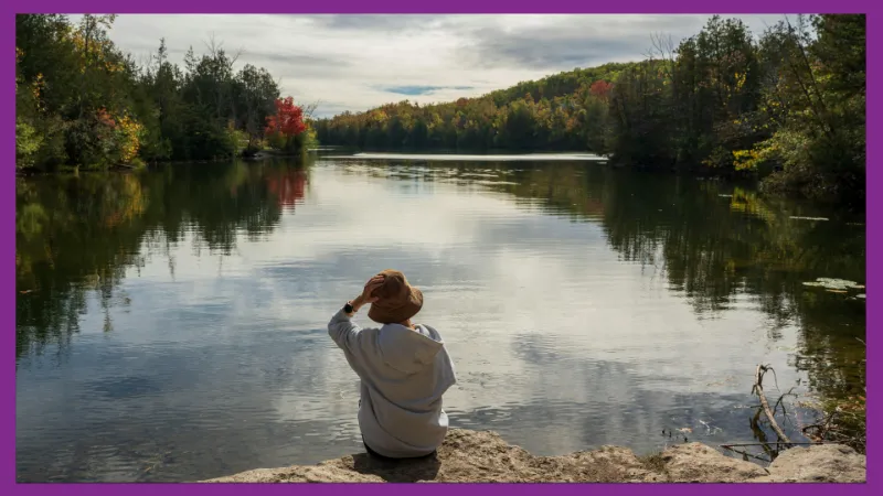 A person sits quietly by a lake, reflecting on their thoughts.