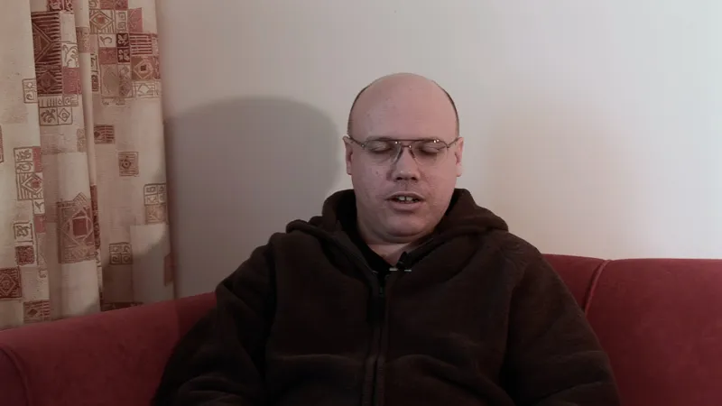 David Thumbnail Sat in a interview with glasses on against a beige background